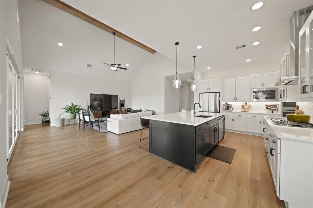 This spacious open-concept living area features high ceilings, a modern kitchen with a large island, sleek cabinetry, and ample natural light. The adjoining living room has stylish wood flooring and a cozy seating area, perfect for entertaining.
