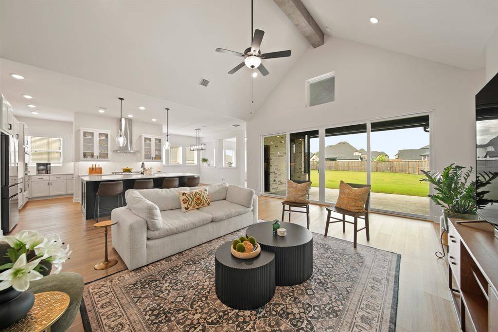 This open-concept living area features a spacious layout with high ceilings and abundant natural light. The modern kitchen boasts an island with seating, while large sliding doors lead to a patio and a well-maintained backyard. Perfect for entertaining and family gatherings.