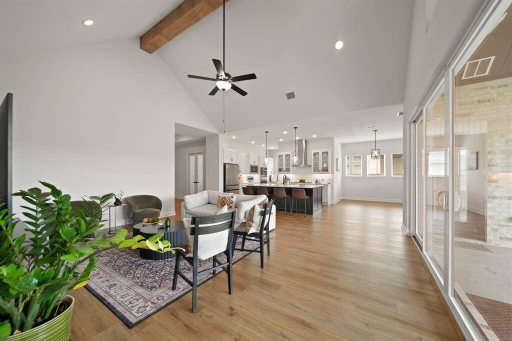 This photo showcases a spacious, open-concept living area with high vaulted ceilings, a cozy seating arrangement, and a modern kitchen with a large island. The space is bright and airy, featuring wood flooring, large windows, and a sliding glass door leading to the outdoor area, creating a seamless indoor-outdoor flow.