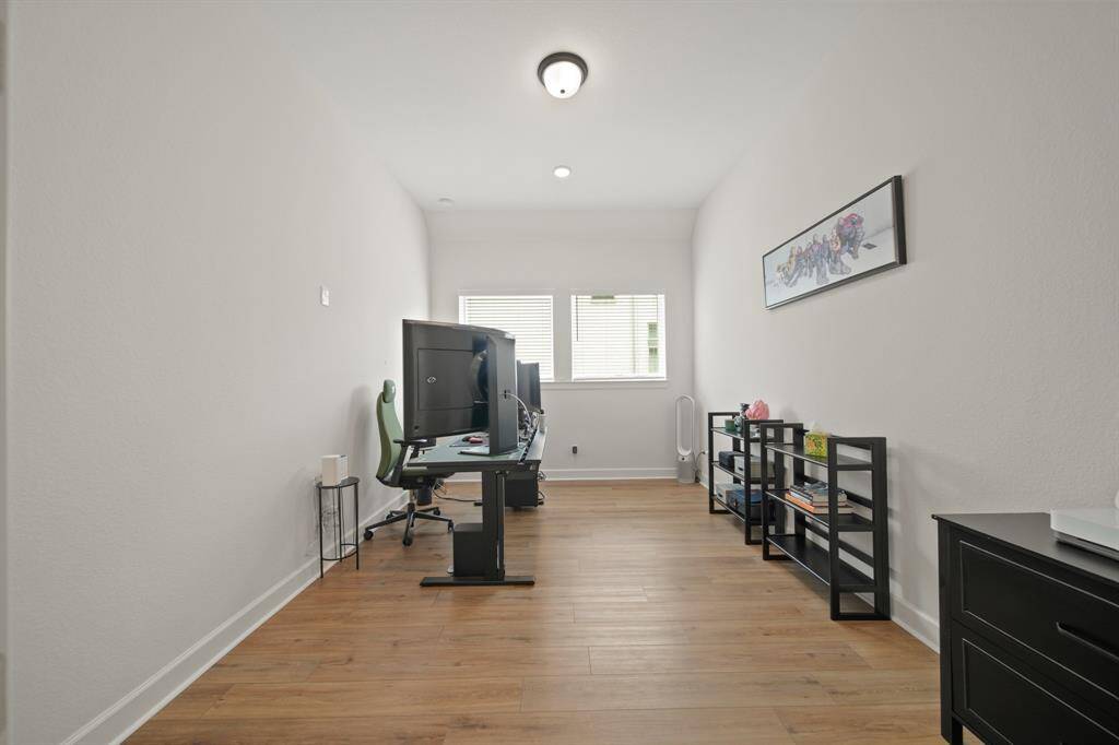 This photo shows a bright home office with wooden floors, natural light, and the room is simply decorated, offering a functional workspace.