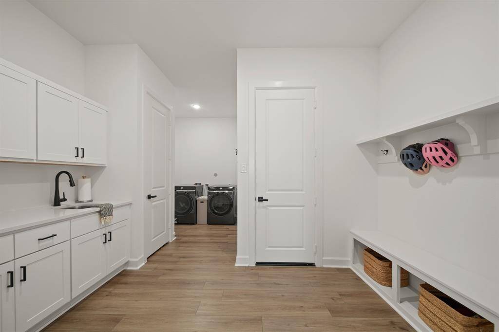 This photo showcases a bright, modern laundry/mudroom with sleek white cabinetry, a built-in sink, and ample storage. The space is stylishly designed with wood flooring and a minimalist aesthetic.