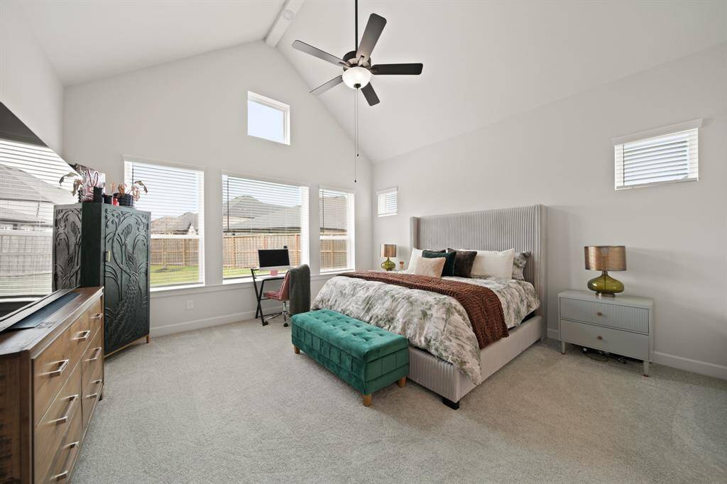 This spacious primary bedroom features high ceilings, ample natural light from multiple windows, and a ceiling fan, creating a comfortable and inviting space.