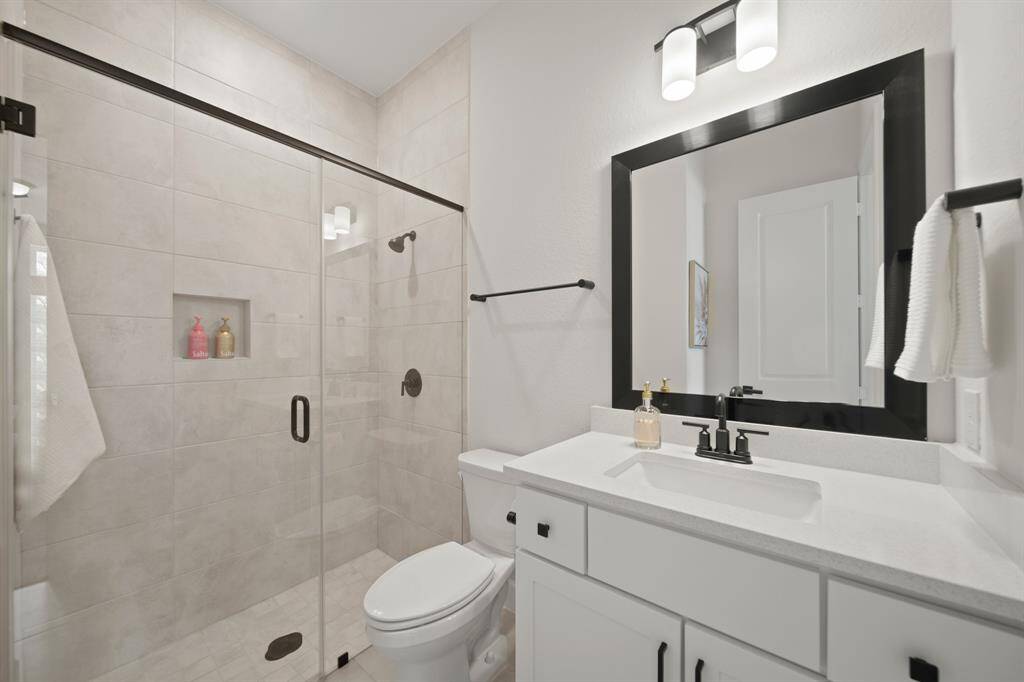 This bathroom features a modern design with a glass-enclosed shower, sleek black fixtures, a white vanity with ample storage, and a large mirror. The neutral color palette and contemporary lighting create a bright and inviting space.