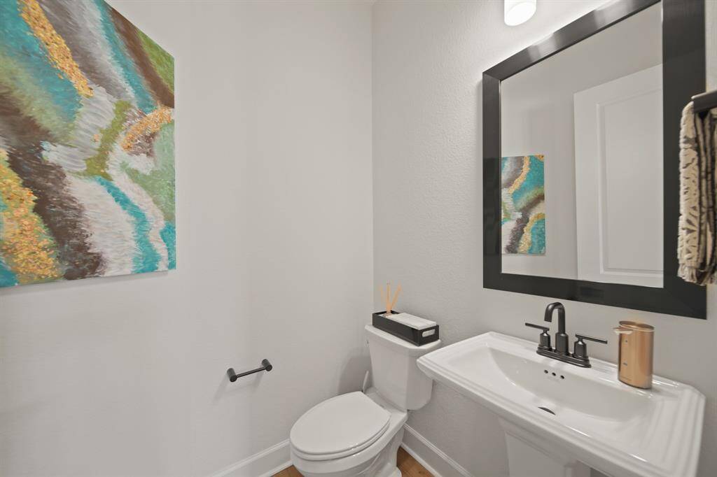 This is a modern, compact bathroom with a sleek pedestal sink, black-framed mirror, and a toilet. The light-colored walls are complemented by a colorful abstract painting, adding a touch of elegance to the space.