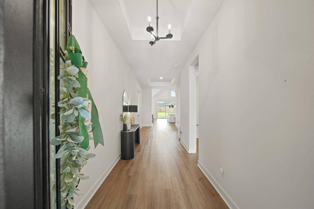 This photo shows a bright, inviting hallway with wood flooring and modern lighting. The hallway leads to a living area with large windows, providing a view of the outdoor space.