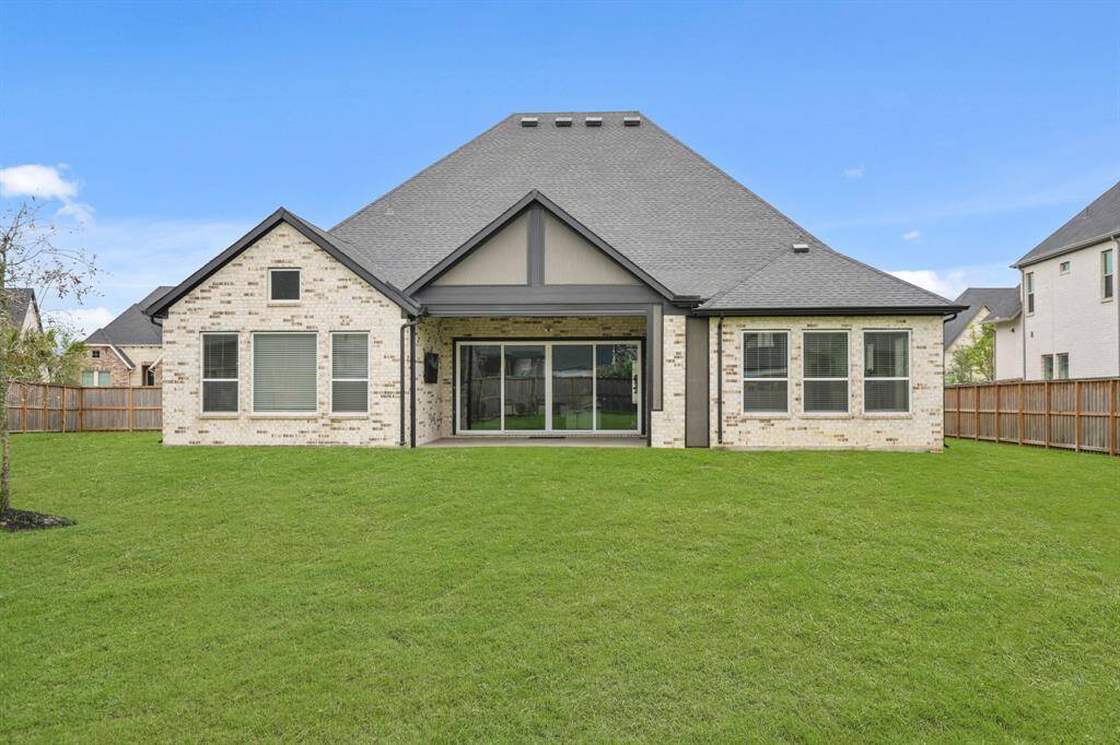 This photo showcases the back of a modern, single-story home with a spacious, well-maintained lawn. It features a light brick exterior, large windows, and a covered patio area with sliding glass doors, ideal for outdoor living and entertainment.