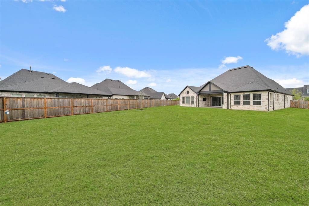 Expansive backyard with well-maintained grass, enclosed by a wooden fence, offering privacy. The house features a modern brick exterior with large windows and a covered patio, perfect for outdoor relaxation.