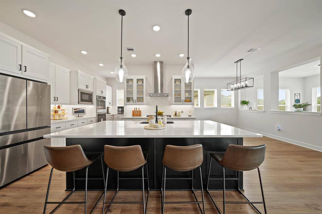 This modern kitchen features a spacious island with sleek stainless steel appliances, and stylish pendant lighting. The open layout is complemented by ample natural light, white cabinetry, and a chic, contemporary design.