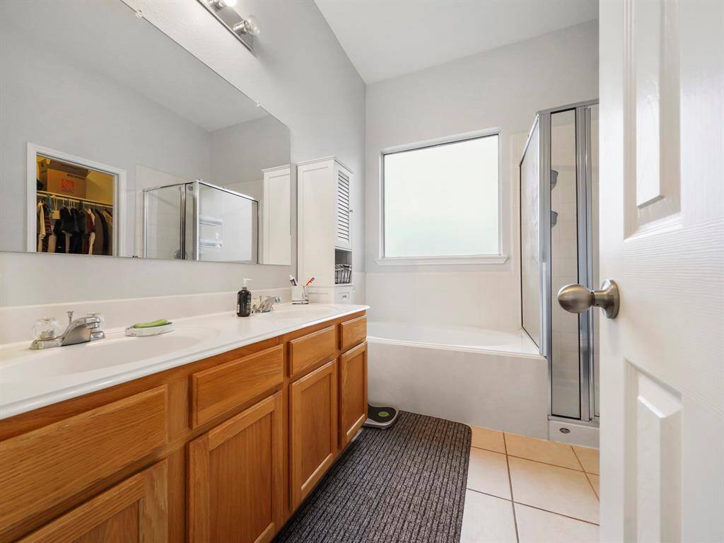 Large primary bathroom has extended vanity with dual sinks, separate shower, soaking tub, and glazed window that allows ample natural light and provides privacy.