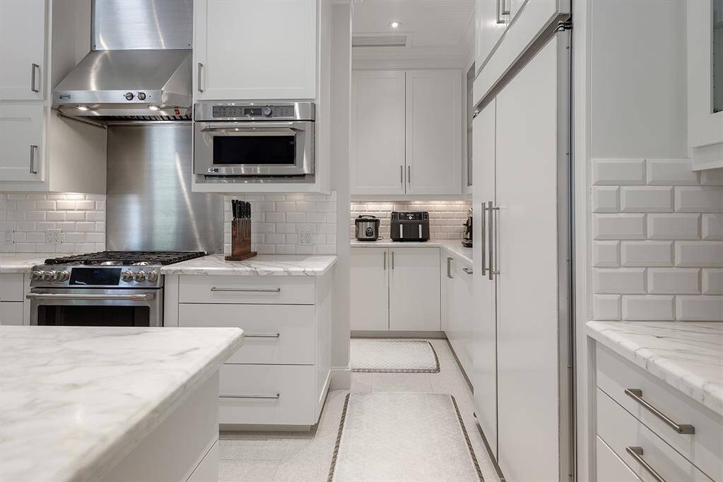 The remodeled island kitchen has honed marble counters, Ann Sacks porcelain limestone tile flooring, a six burner gas range with vent hood, glass front cabinetry and warming drawer.