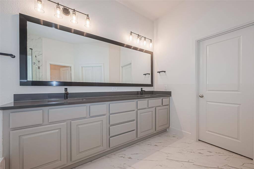 This stunning double vanity has a sleek surface, oversized mirror, modern lighting and fixtures.