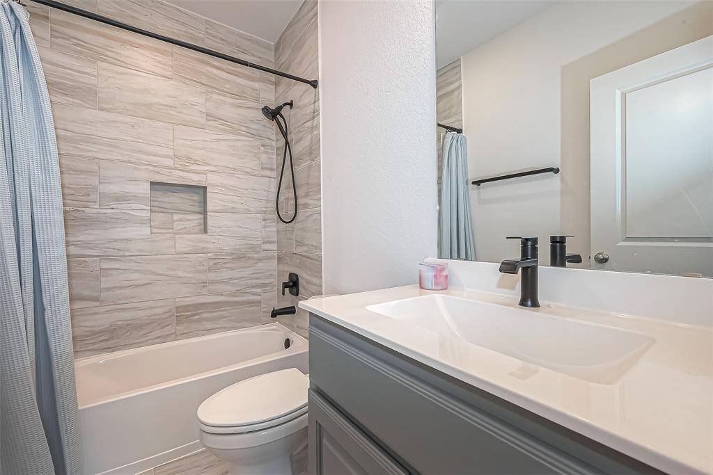 The secondary bathroom boasts tiled shower surround up to the ceiling, recessed niche, and matte black fixtures.