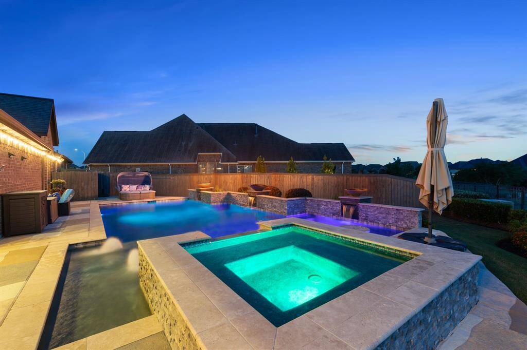 This covered outdoor kitchen and lounge area shines at night with string lights, built-in grill, and multiple seating options—perfect for hosting under the stars.
