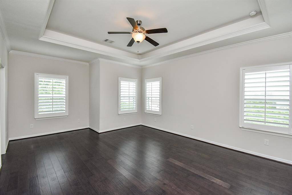 The expansive primary bedroom features a tray ceiling, multiple windows, and delicate crown molding—creating a space that feels both relaxed and refined.