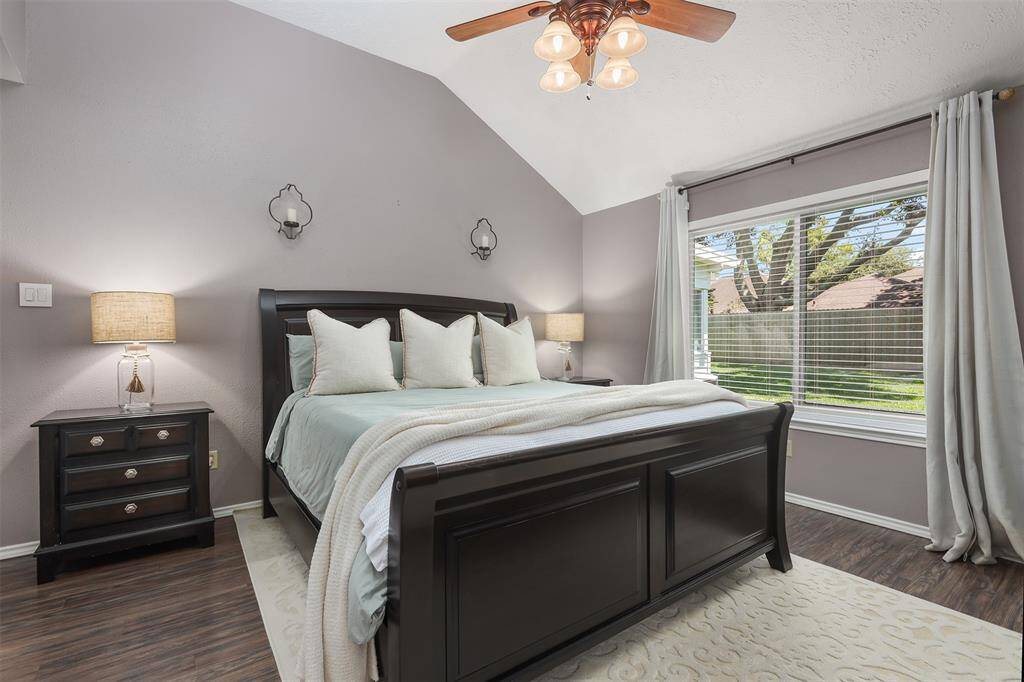 This inviting Primary bedroom features a high ceiling with a fan, ample natural light from a large window, and a cozy atmosphere. The soft color palette provides a serene and comfortable setting.