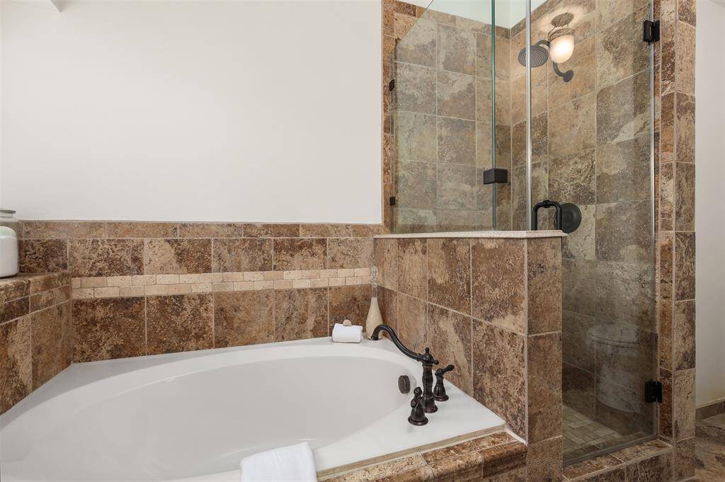 This Primary bathroom features a luxurious stone-tiled design with a spacious soaking tub and a glass-enclosed shower.