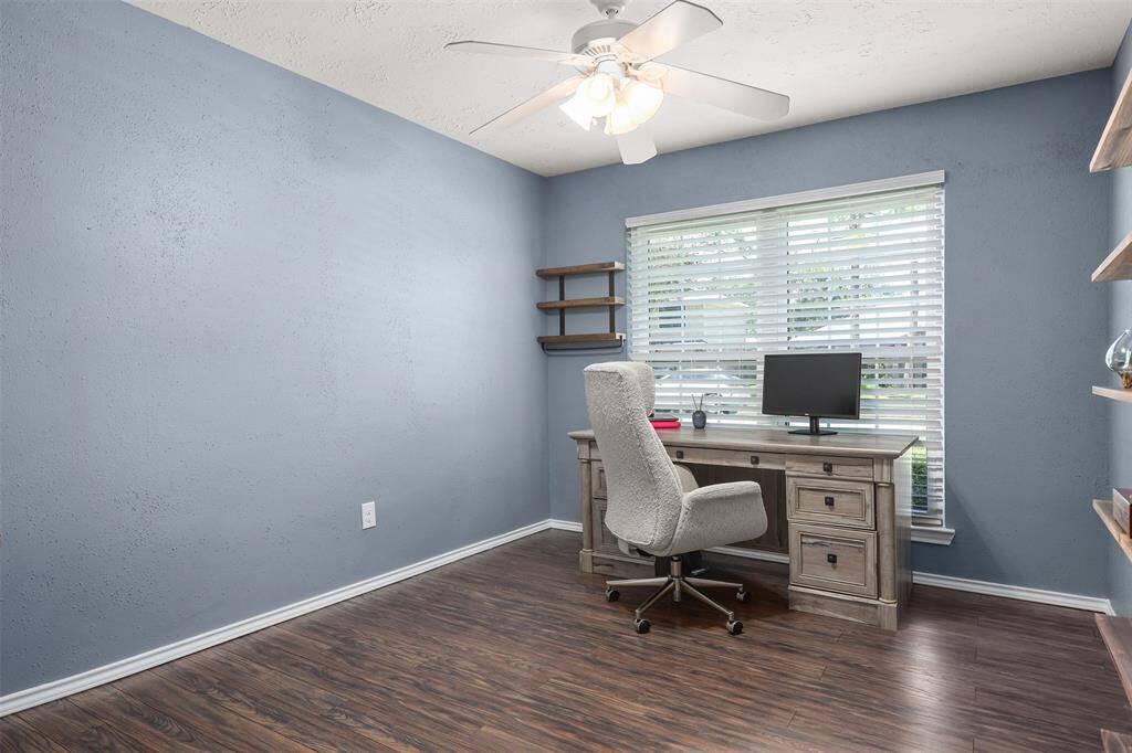 This cozy home office or third bedroom features soothing blue walls, "wood like" flooring, ceiling fan, closet and ample natural light from a large window with blinds.