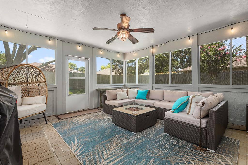 Bright, screened in sunroom, featuring a cozy seating area with a paver floor. The space includes a ceiling fan perfect for relaxing, entertaining or just enjoying nature in the beautiful backyard.
