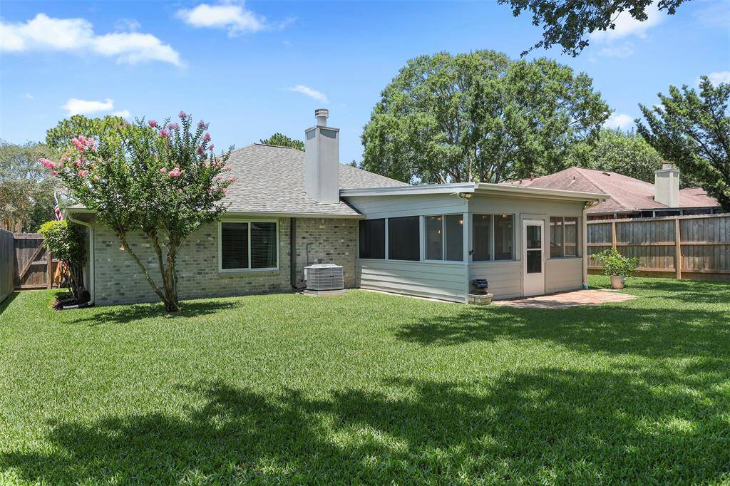 This photo showcases a well-maintained backyard featuring a lush green lawn, mature trees, and the attached screened-in sunroom. The area is fenced and provides privacy and a great space for outdoor activities.