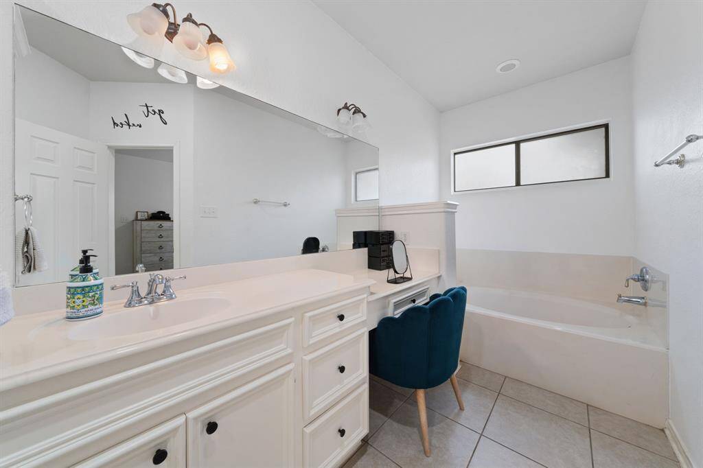 WOW! Spacious Primary Bathroom, featuring tile flooring, large mirror, elegant lighting, a vanity area, white cabinets, granite countertops, soaking tub, and a window with privacy glass.