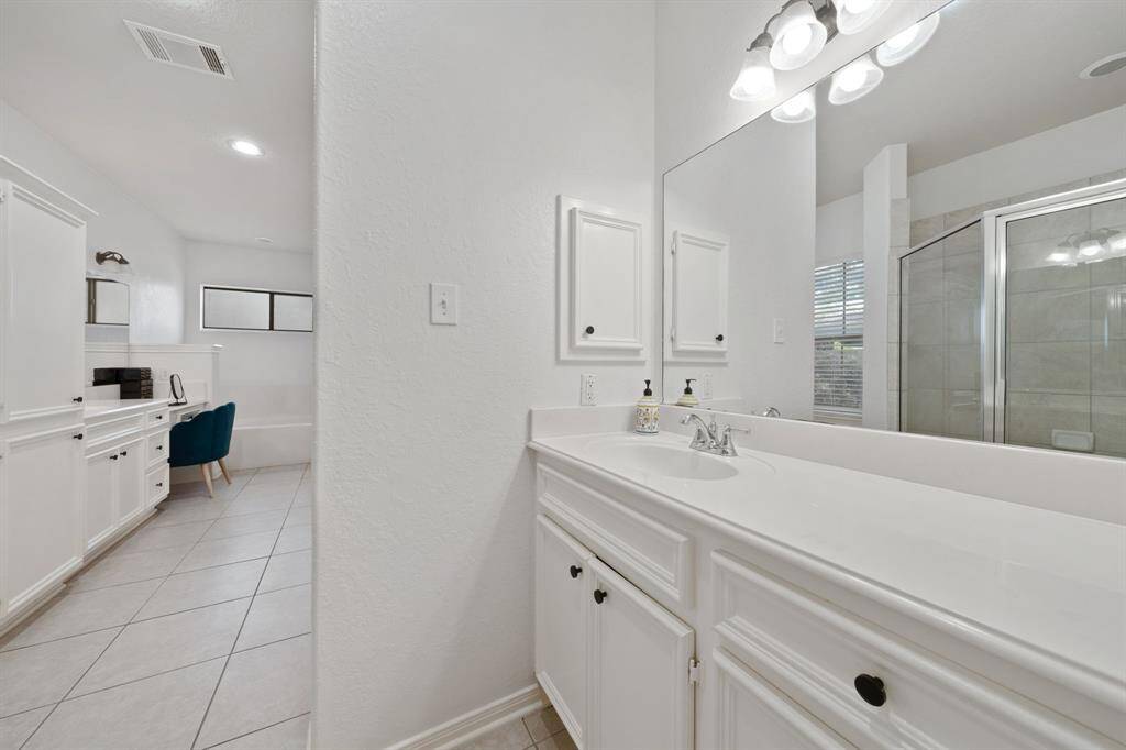 This Primary Bathroom features separate sinks with white cabinetry, a large mirror and vanity lights.