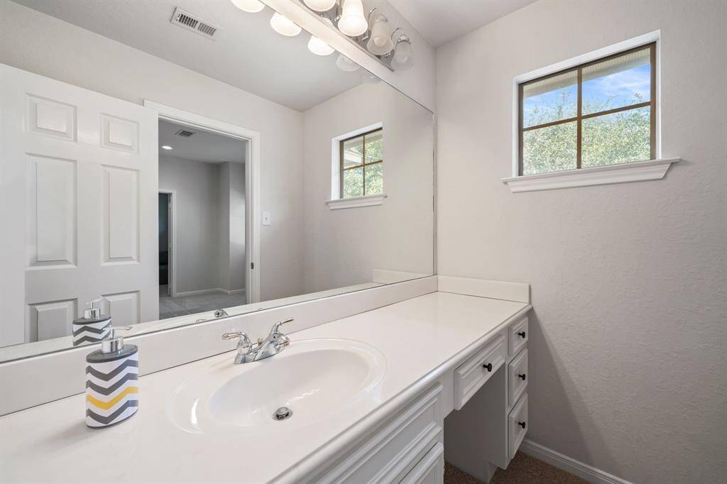 Beautiful secondary bathroom featuring white cabinetry, granite countertops, a vanity area, large mirror, and vanity lights.