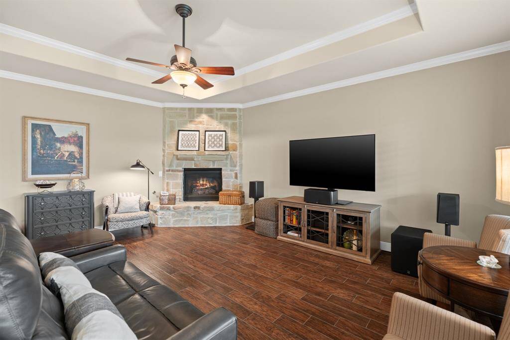 The corner stone fireplace is a stunning focal point, adding rich texture and character with its unique hearth. Above, a tray ceiling with double crown molding creates a bright, airy atmosphere that elevates the entire space.