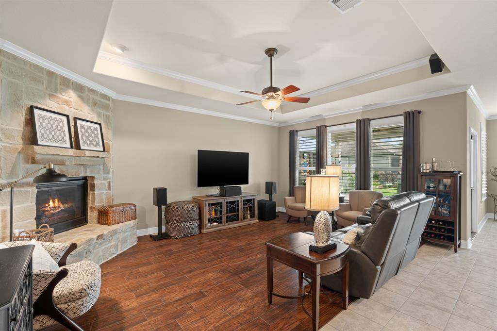 This room feels warm and welcoming, with rich wood-tone tile flooring, a graceful tray ceiling, and charming shutters that add a touch of classic elegance.