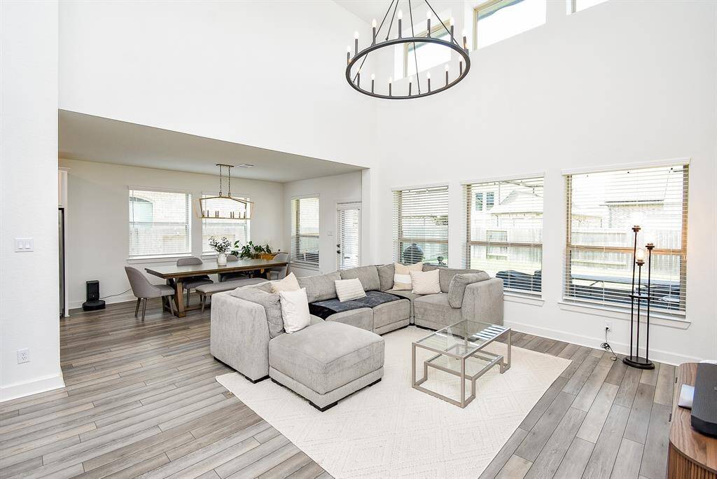 Soaring ceilings and two tiers of windows flood the living room with light, while a sculptural black chandelier offers contrast against the neutral palette of white walls and light wood floors.