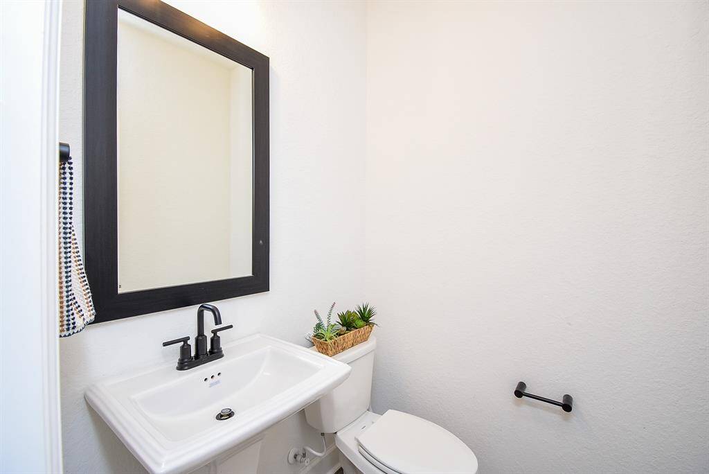 The half bath features a pedestal sink, black hardware, and a sleek mirror framed in matte black—simple, yet striking in its monochromatic elegance.