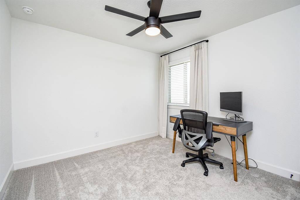 Carpeted comfort meets versatility in this light-filled bedroom. A ceiling fan and large window make it a perfect space to wind down or focus up.