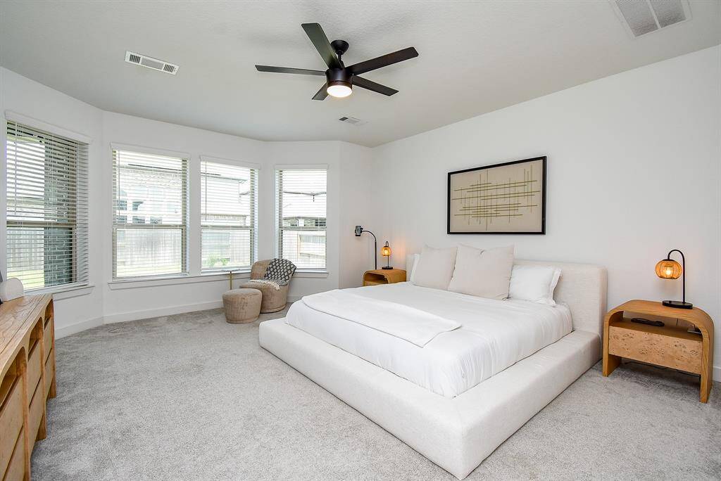 Soft carpeting and a curved wall of tall windows give this serene primary bedroom its sense of scale and softness.