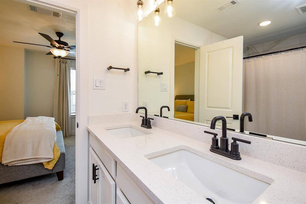 Streamlined finishes and a clean design define the en suite, featuring dual sinks, black fixtures, and a full-width frameless mirror.