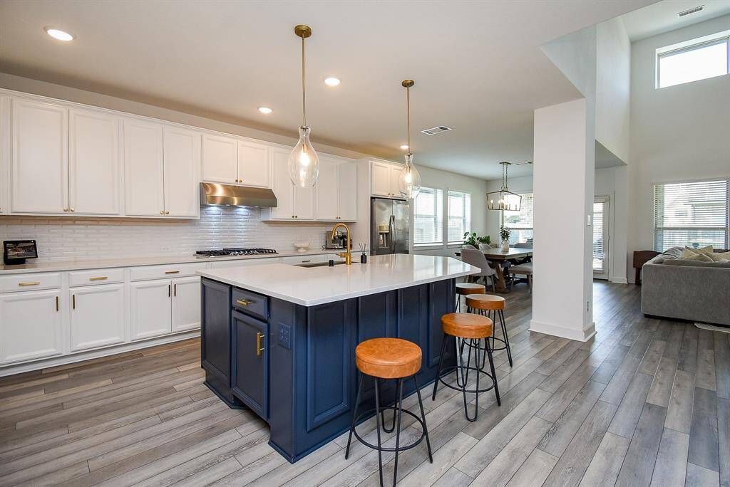 The kitchen features a deep blue base cabinetry under the island, crisp white upper and lower cabinets, and complementing countertops. Pendant lights add a soft glow above the island seating, perfect for casual conversations.