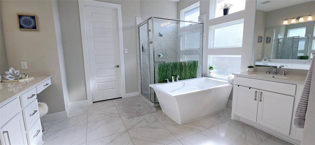 Primary Bath room luxurious ready for relaxation and functionality. features a spacious layout with two separate vanity areas each one with a sink, complete with elegant countertops. A large glass walk-in shower and a freestanding soaking tub high-end tile flooring