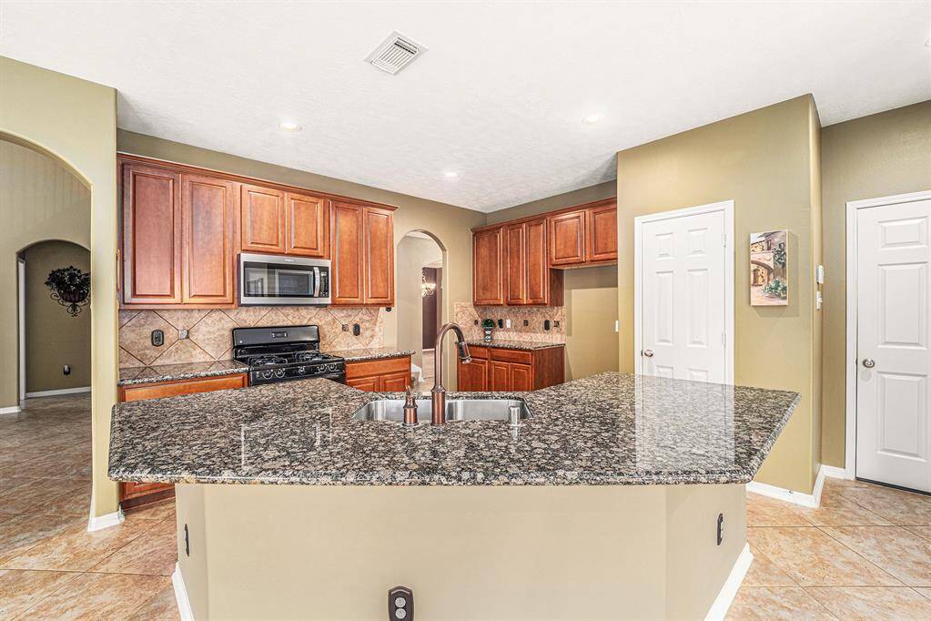 A spacious island kitchen awaits the chef of the home!  Gorgeous granite sits atop warm stained cabinets, and a custom backsplash creating a warm environment to enjoy a glass of wine, while the chef of the home whips up some meals!