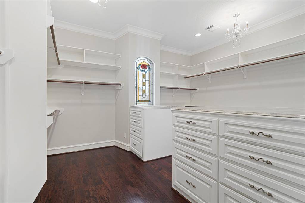 The primary walk-in closet has high ceilings, crown molding, chandeliers, stained glass window, and plenty of storage space.