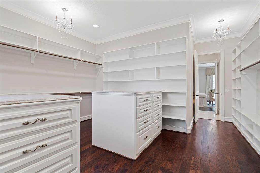 The primary walk-in closet has high ceilings, crown molding, chandeliers, stained glass window, and plenty of storage space.