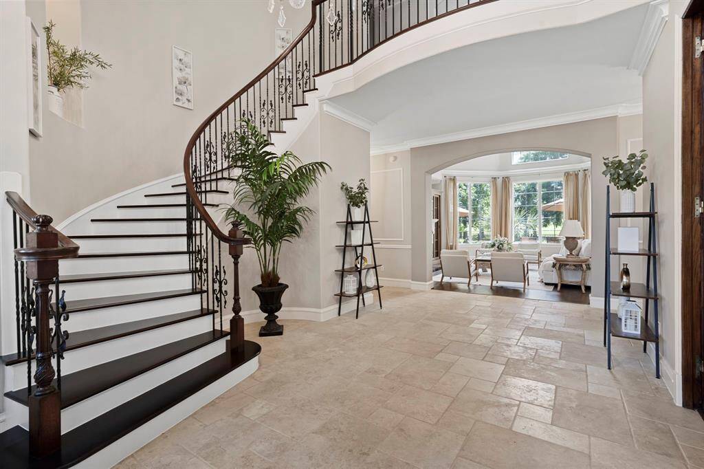The foyer boasts highceilings and is adorned with tastefuldecor, curved staircase with iron railing details, tile floors, and chandelier lighting, creating an immediate senseof elegance.
