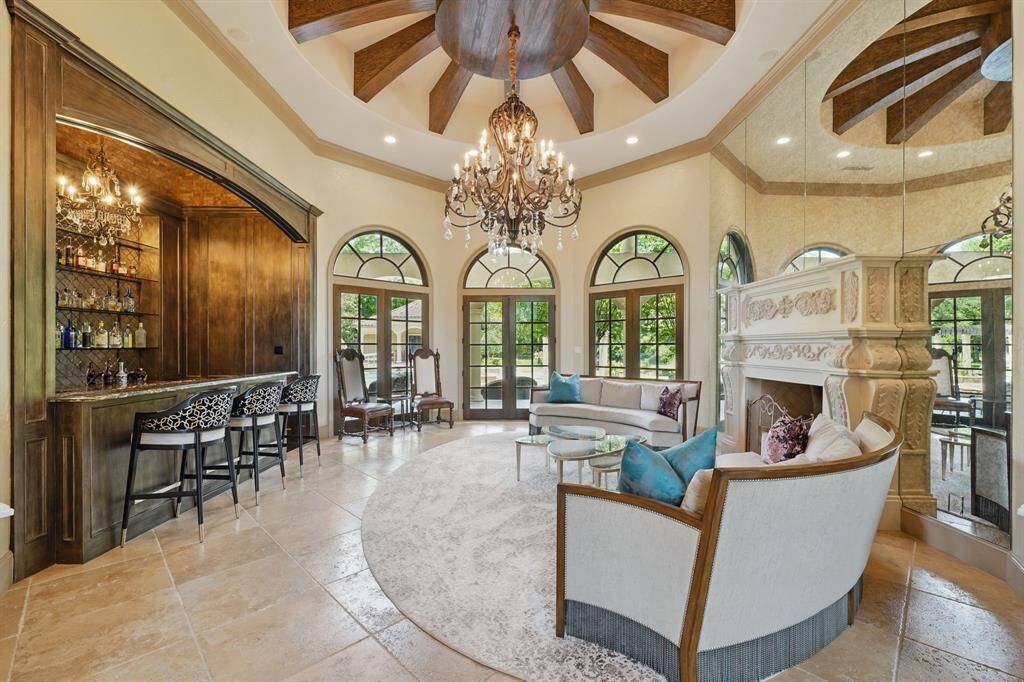 The family room features tile floors, chandelier lighting, wall of mirrors, cozy fireplace, large windows, and a wet bar.