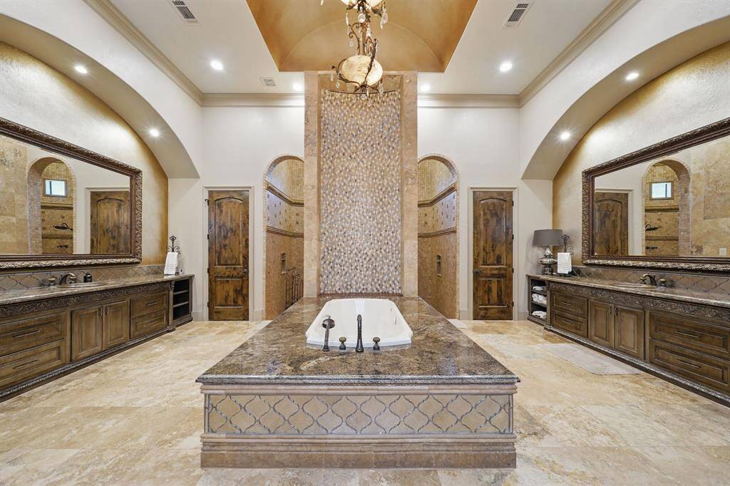 The primary bathroom features tile floors, dual sinks, soaking tub with chandelier above, dual water closets, and huge walk-in shower with tile surround.