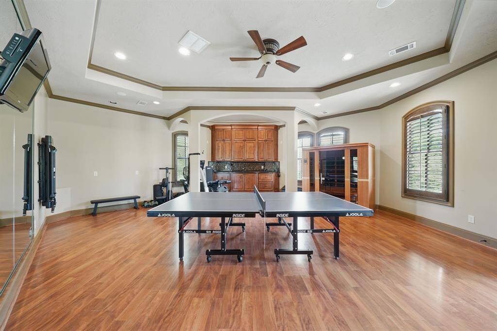The exercise room features large mirrors, high ceilings, recessed lighting, ceiling fan, and large windows with shutters.