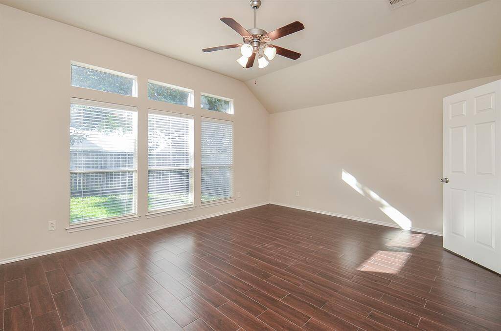Primary bedroom with three large windows allowing abundant natural light and stylish wood-look flooring.