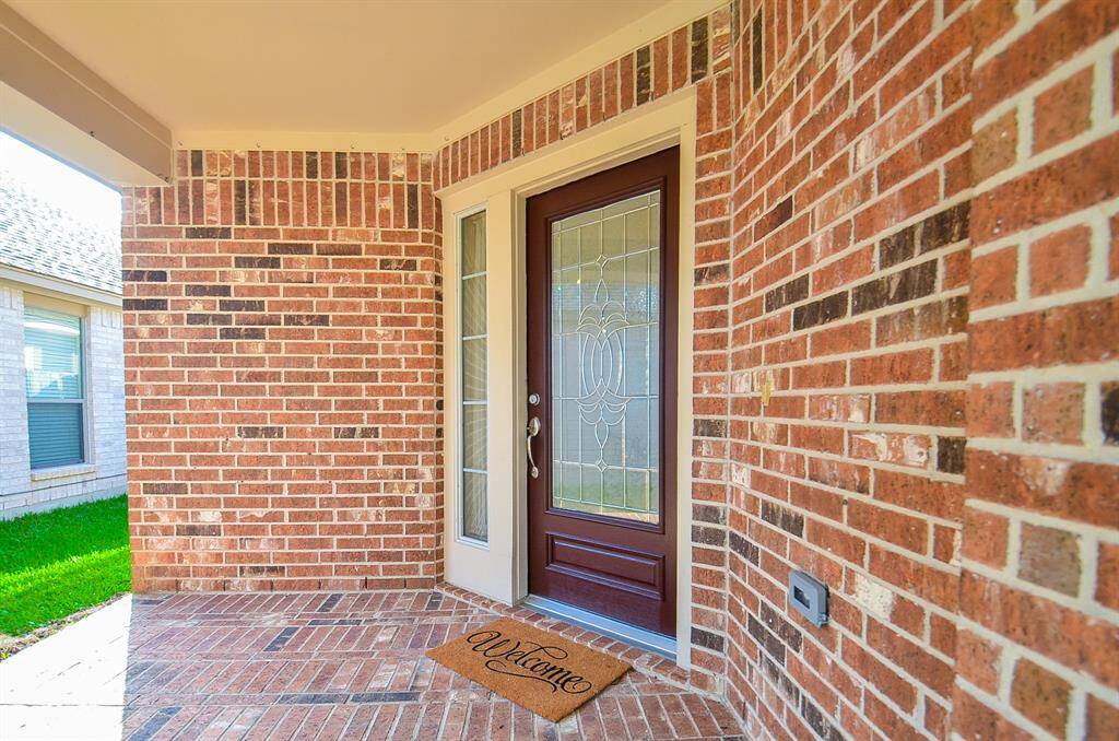 Elegant brick exterior surrounds the inviting front entrance, featuring a stylish wood and glass front door with decorative wrought iron detail.