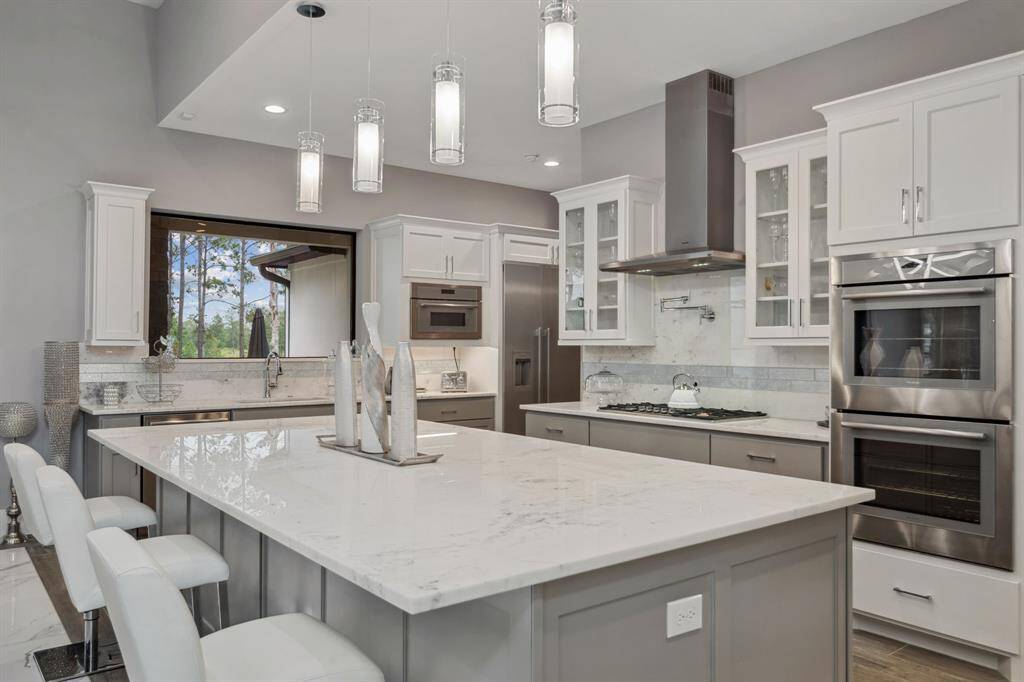 Enhanced by ample lighting, striking pendant fixtures, and a bold statement piece, this kitchen exudes a unique and stylish charm.