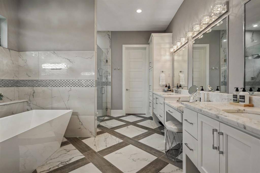 A spacious, elegantly designed bathroom featuring a standalone tub, unique fixtures, an oversized shower, dual sinks, and vanity.