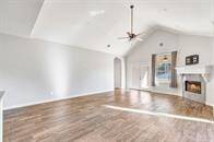 This is a spacious, well-lit living room with high vaulted ceilings, hardwood tile floors, a cozy fireplace, and French doors leading to an outdoor area.
