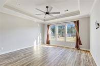 This is a spacious primary bedroom with well-lit room featuring vinyl floors, large windows with a view of the yard, and a ceiling fan. The tray ceiling adds an elegant touch to the space.