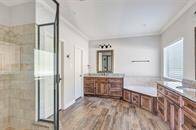 Modern bathroom featuring a glass-enclosed shower, a built-in bathtub, wooden vanity with granite countertops, and tiled flooring. Natural light enters through the window, enhancing the bright, airy feel.