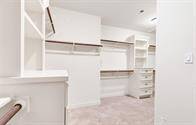 This is a walk-in closet with built-in shelves, drawers, and hanging rods, featuring plush carpeting